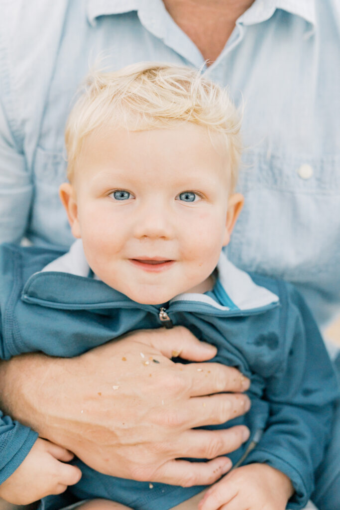 Boy in fathers lap during a beach family session by Jacksonville Family photographer